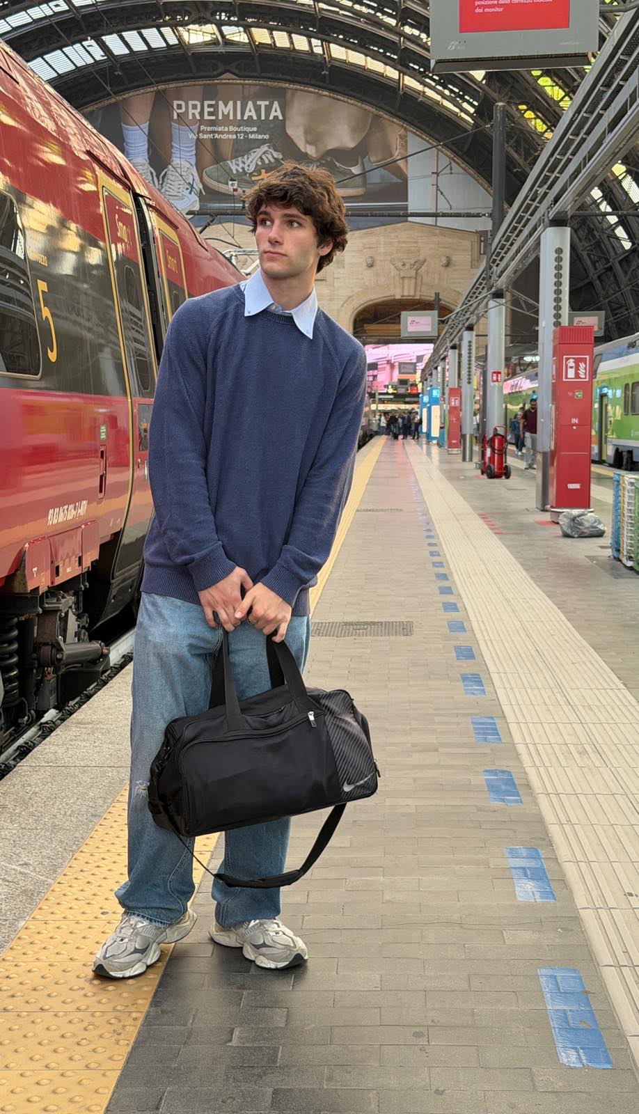 Jack on a platform at Milano Centrale, a red high-speed train beside him and the station's arched hall behind.