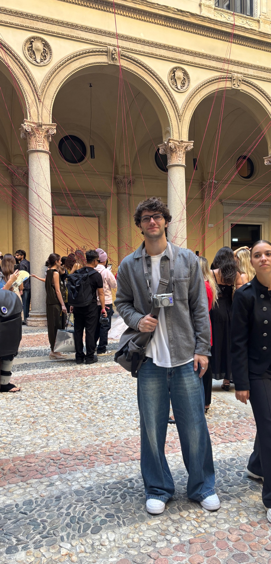 Jack with a camera in a Milan palazzo courtyard, red threads strung between the arches behind him.